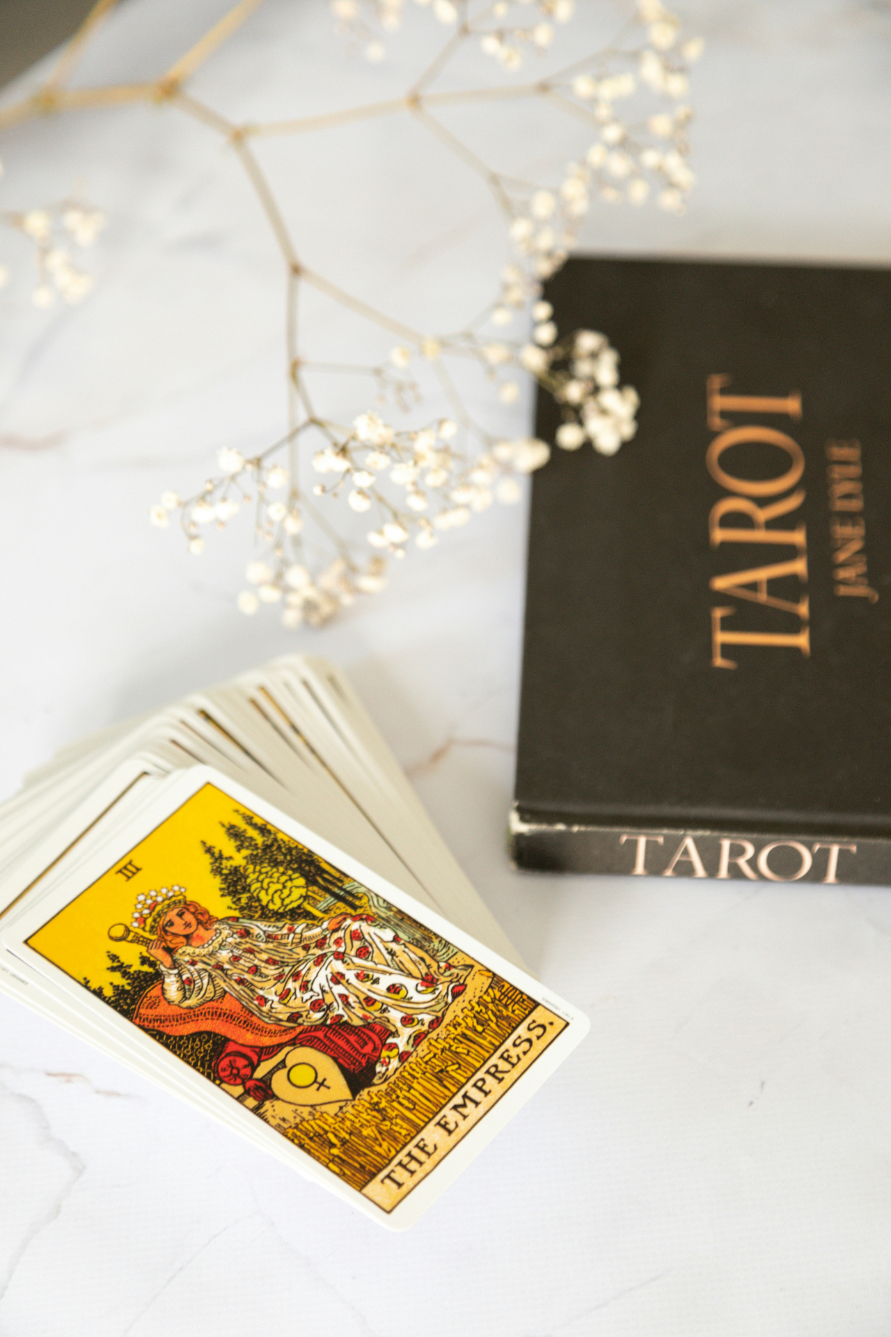 tarot-kortstokk med Keiserinne-kortet ved siden av en tarot-bok og tørkede blomster
